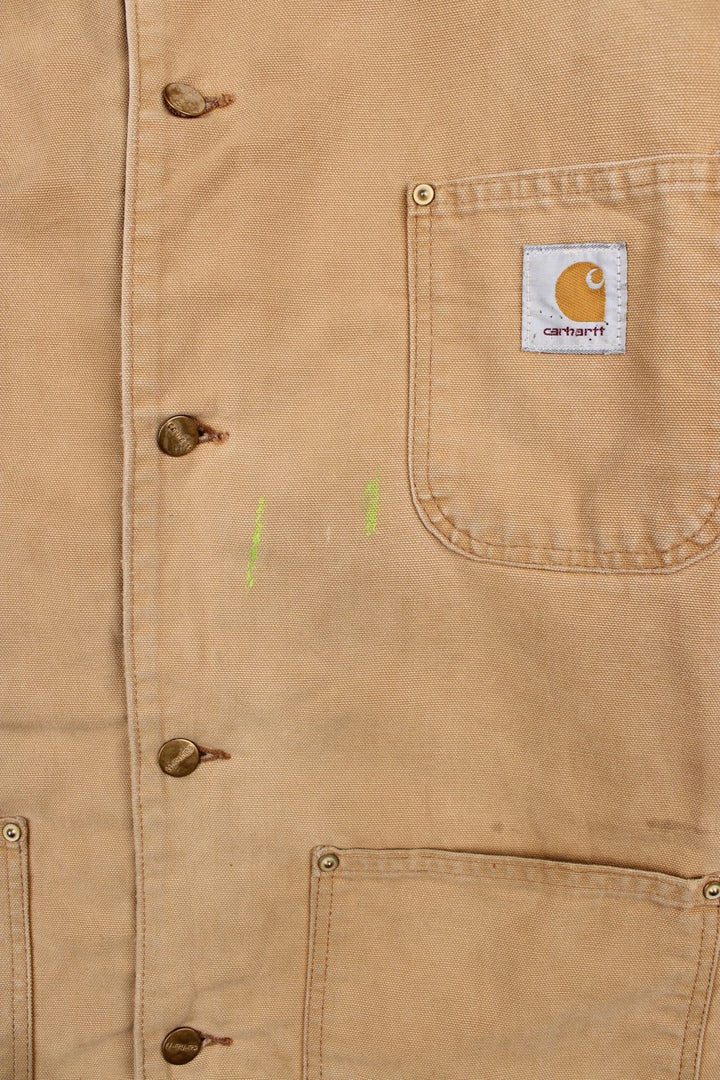 Carhartt Chore Jacket in a tan colourway with a brown corduroy collar. Buttons up and has multiple pockets, blanket lining, and has the logo embroidered on the front.