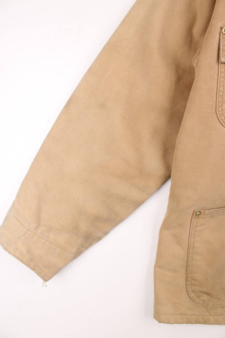 Carhartt Chore Jacket in a tan colourway with a brown corduroy collar. Buttons up and has multiple pockets, blanket lining, and has the logo embroidered on the front.