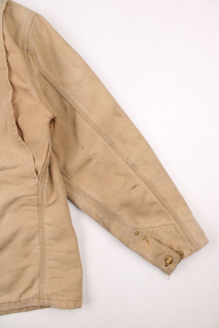 Carhartt Chore Jacket in a tan colourway with a brown corduroy collar. Buttons up and has multiple pockets, blanket lining, and has the logo embroidered on the front.