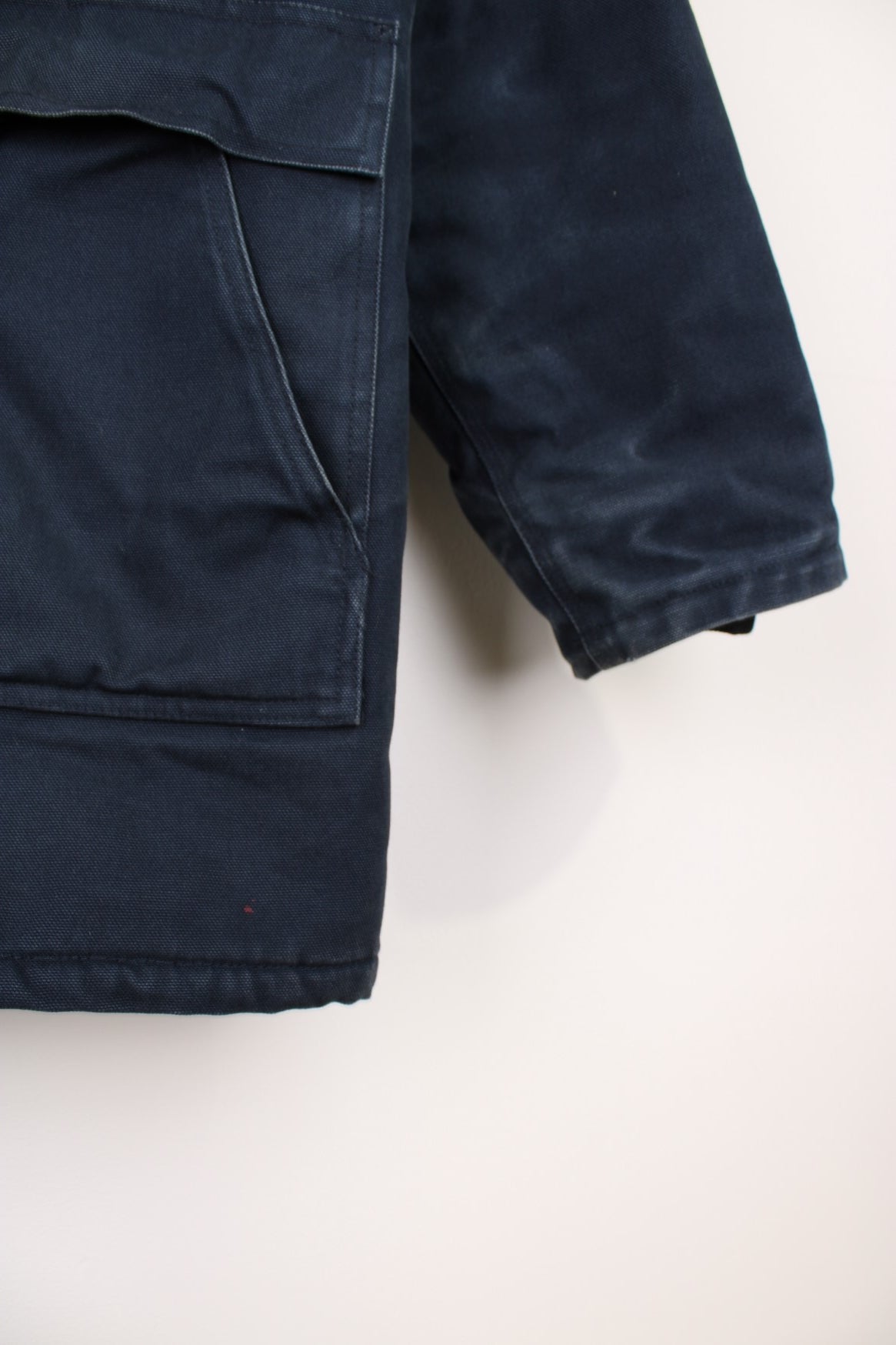 Carhartt Parka Coat in a navy blue colourway, zip up with multiple pockets, insulated with a quilted lining, has a faux fur hood, and the logo embroidered on the front. 