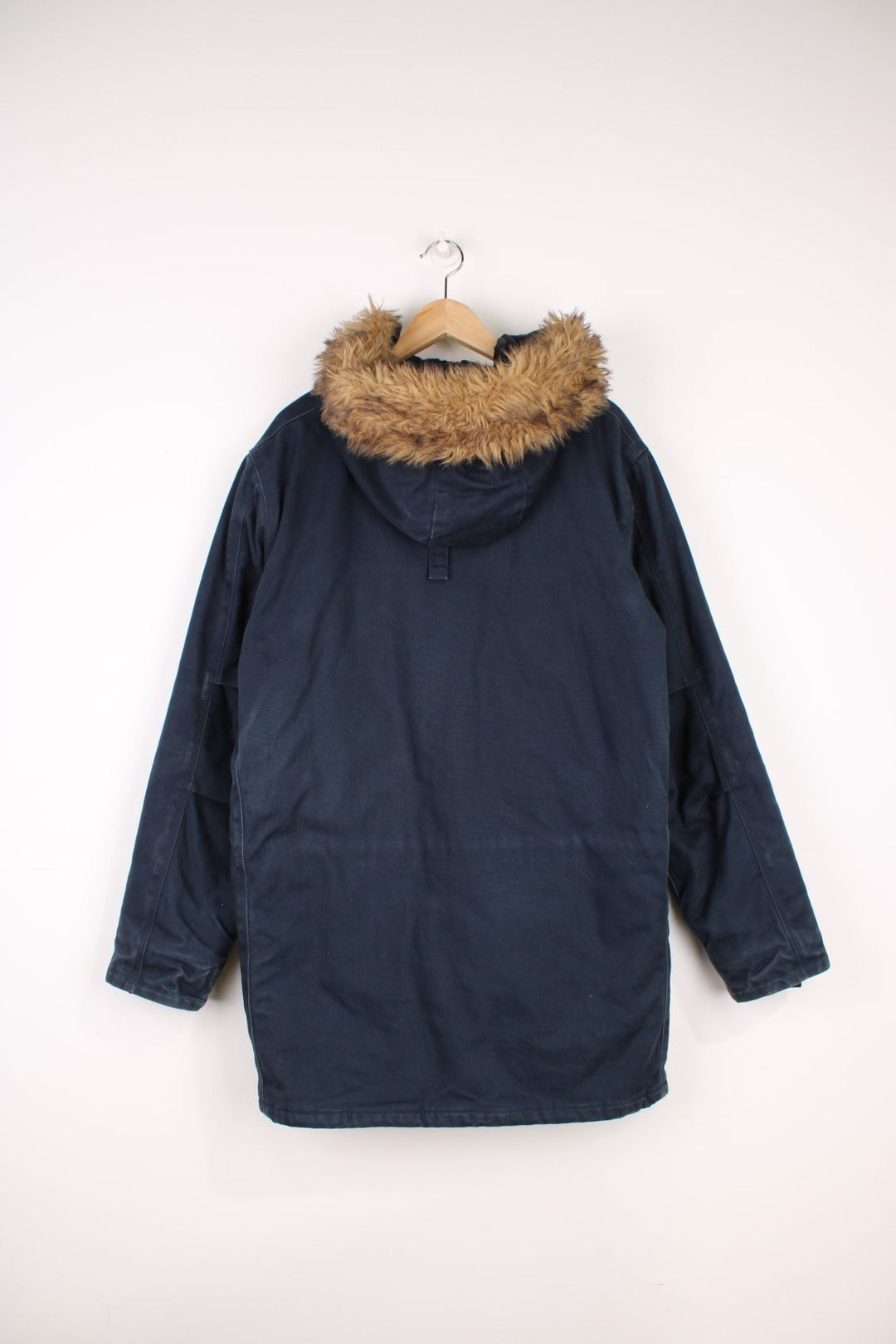 Carhartt Parka Coat in a navy blue colourway, zip up with multiple pockets, insulated with a quilted lining, has a faux fur hood, and the logo embroidered on the front. 