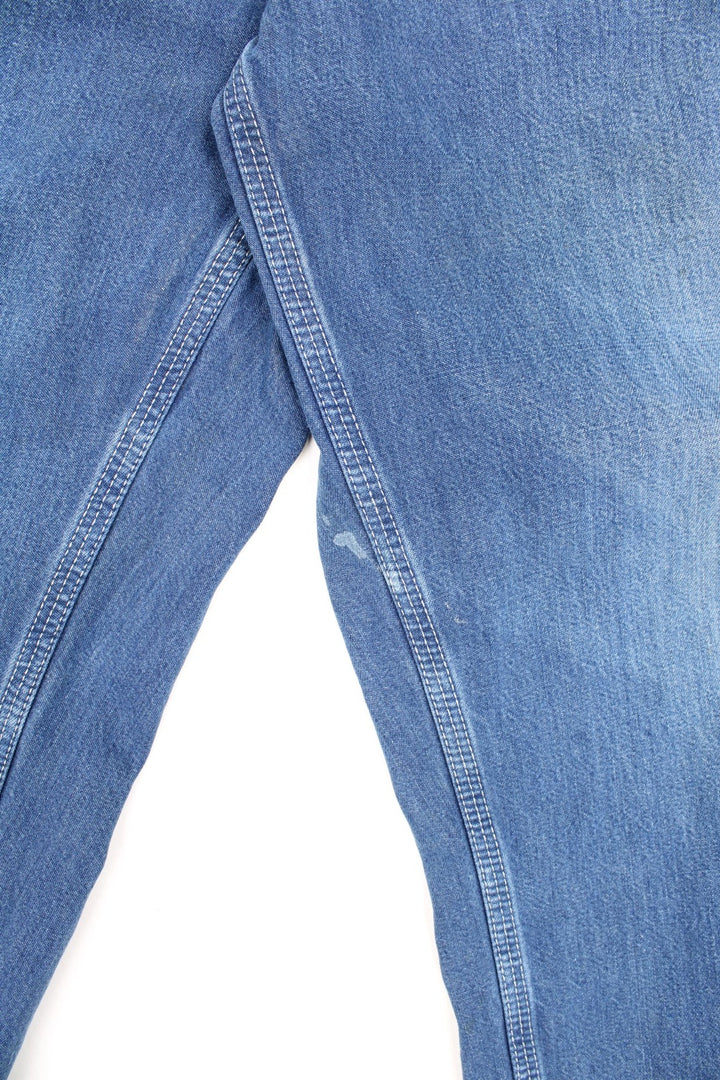 Carhartt Carpenter jeans in a faded blue denim, with white contrast stitching, multiple pockets and the logo embroidered on the back.