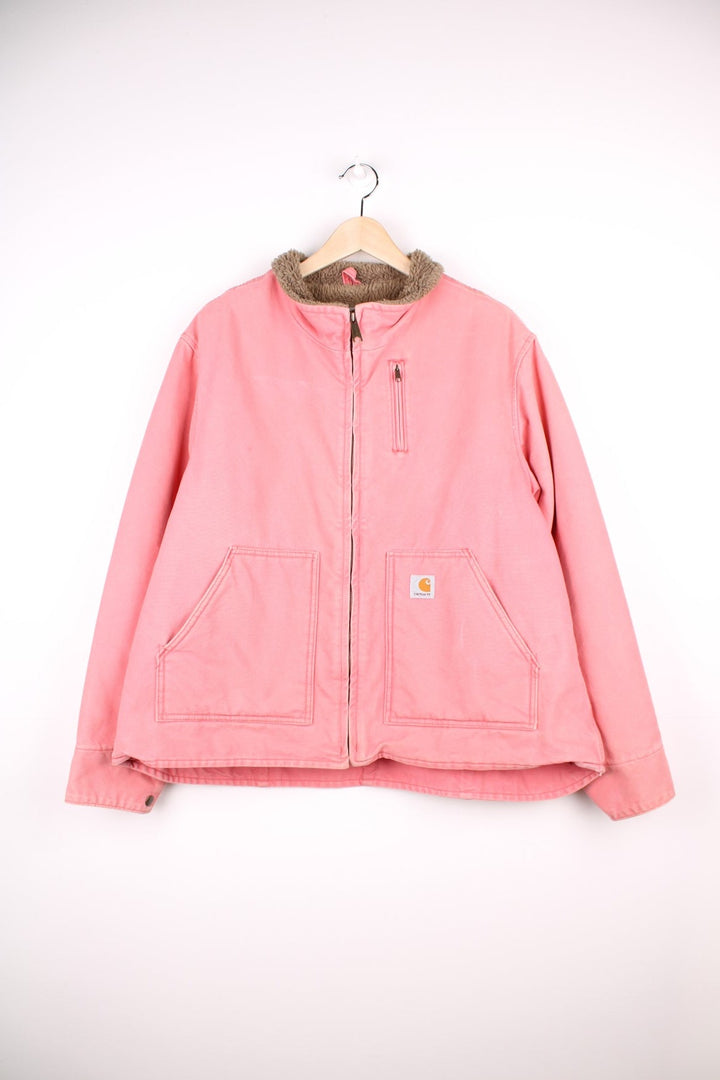 Carhartt Workwear Jacket in a pink colourway with a brown sherpa lining, zips up with multiple pockets, and has the logo embroidered on the front. 