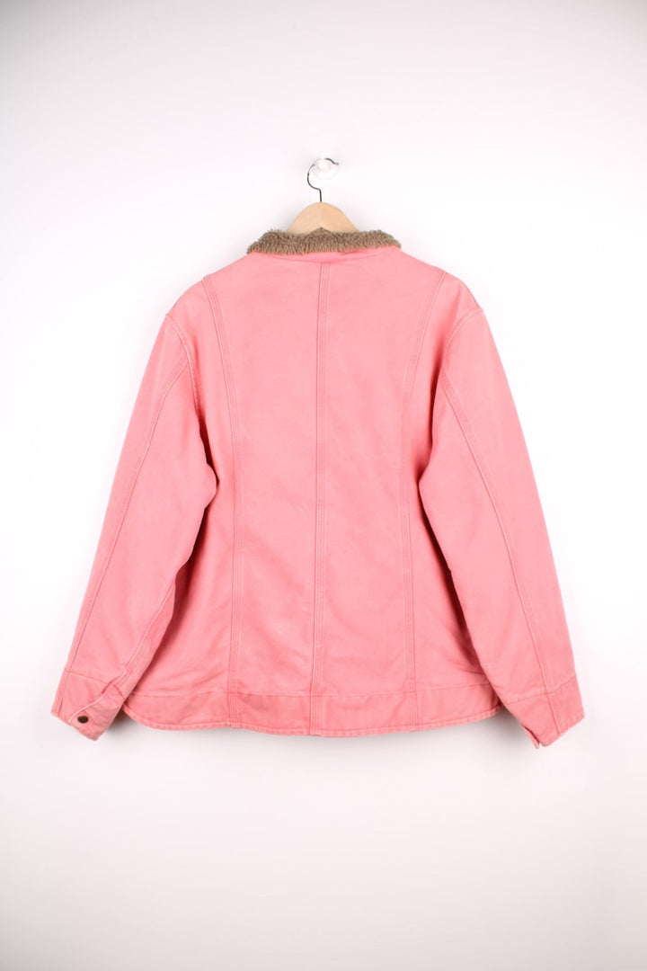 Carhartt Workwear Jacket in a pink colourway with a brown sherpa lining, zips up with multiple pockets, and has the logo embroidered on the front. 