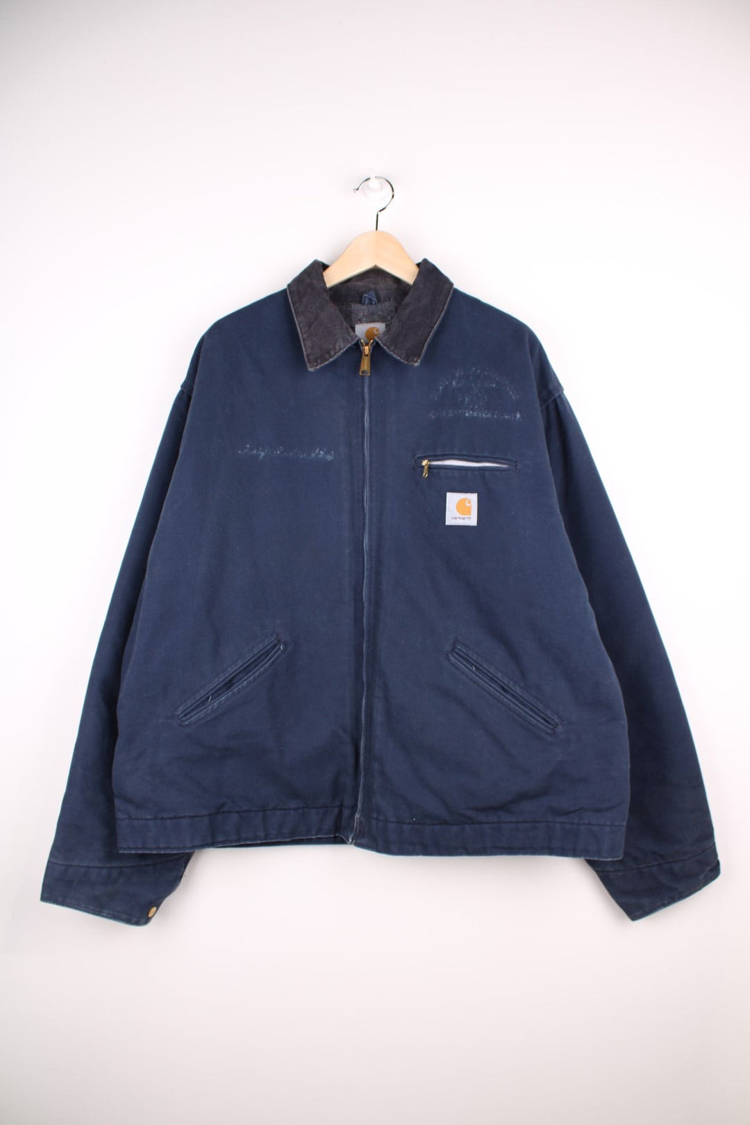 Carhartt Detroit Jacket in a navy blue colourway with a brown corduroy collar, zips up and has multiple pockets, blanket lining, and the logo embroidered on the front. 