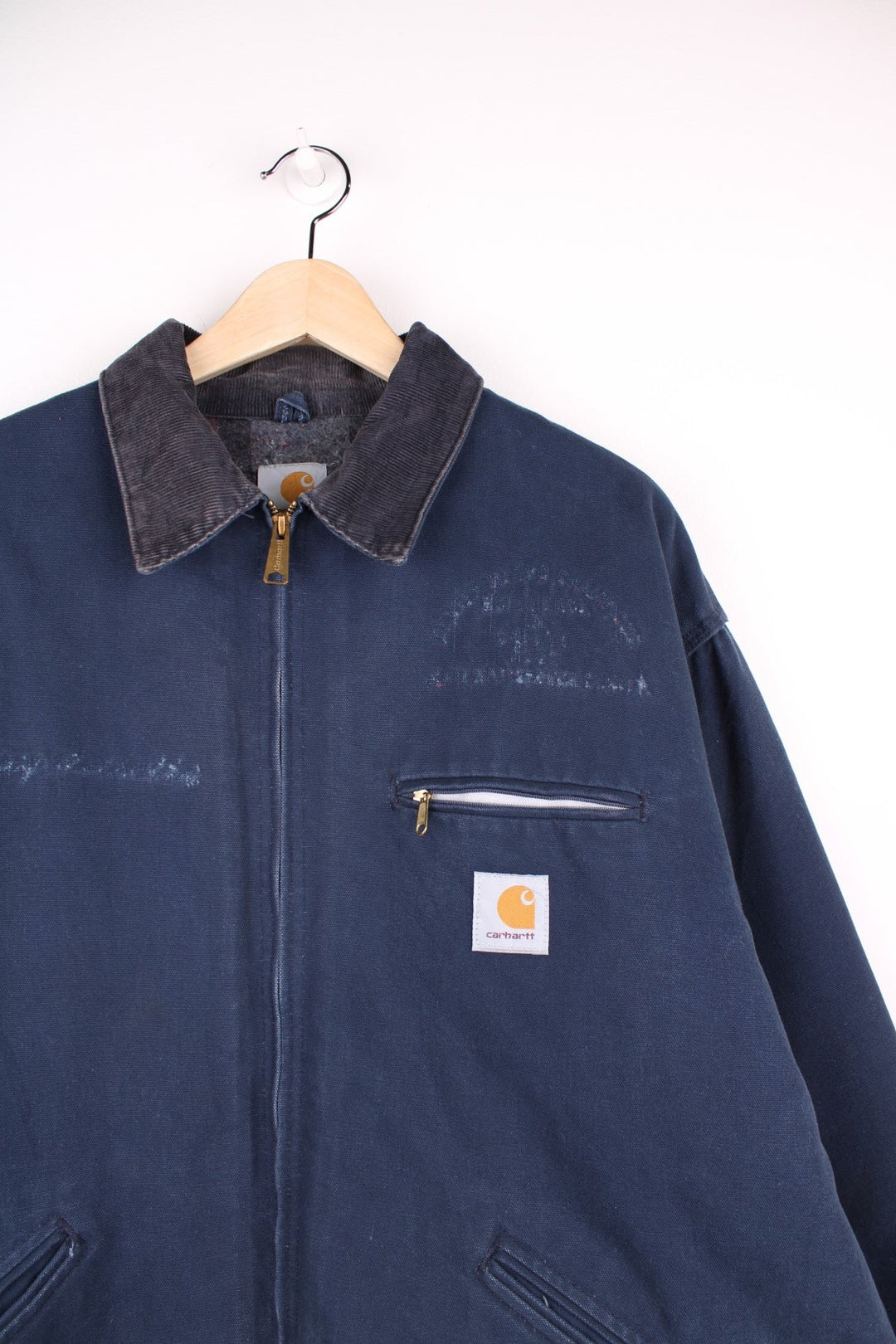 Carhartt Detroit Jacket in a navy blue colourway with a brown corduroy collar, zips up and has multiple pockets, blanket lining, and the logo embroidered on the front. 