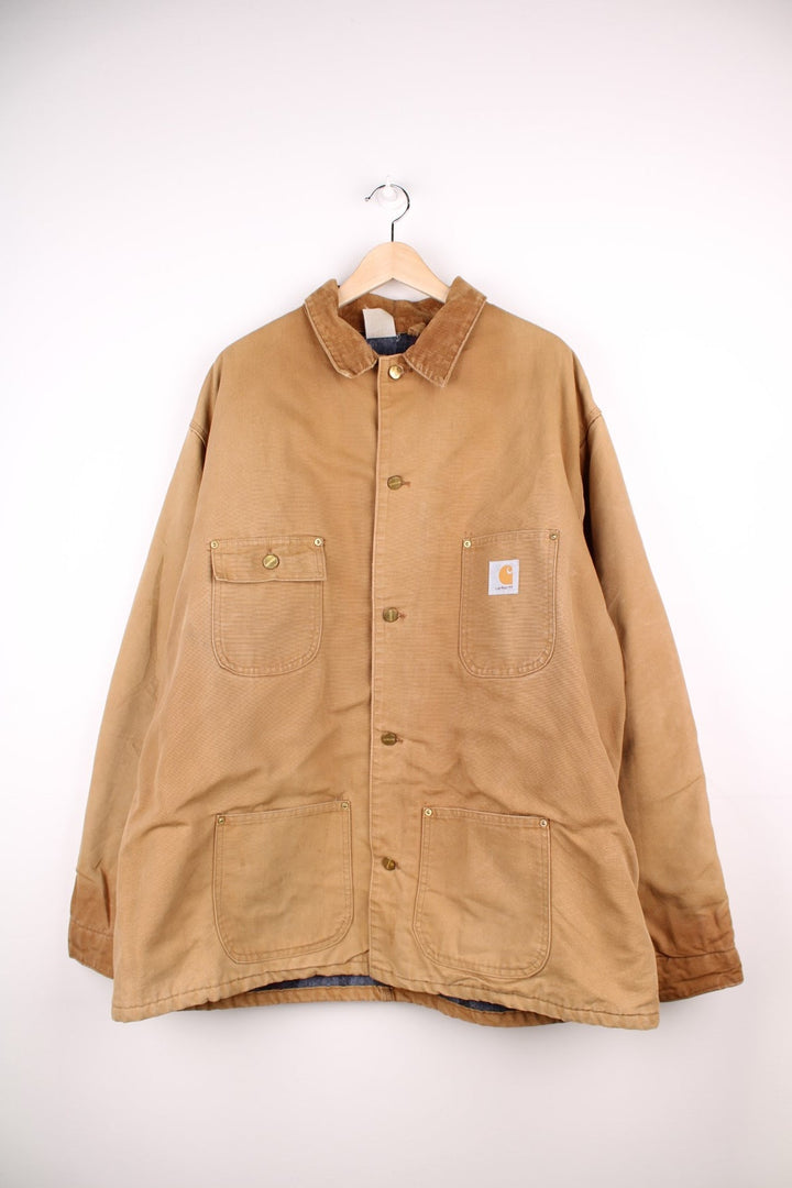 Carhartt Chore Jacket in a tanned colourway with a corduroy collar, buttons up and has multiple pockets, blanket lining, and the logo embroidered on the front. 