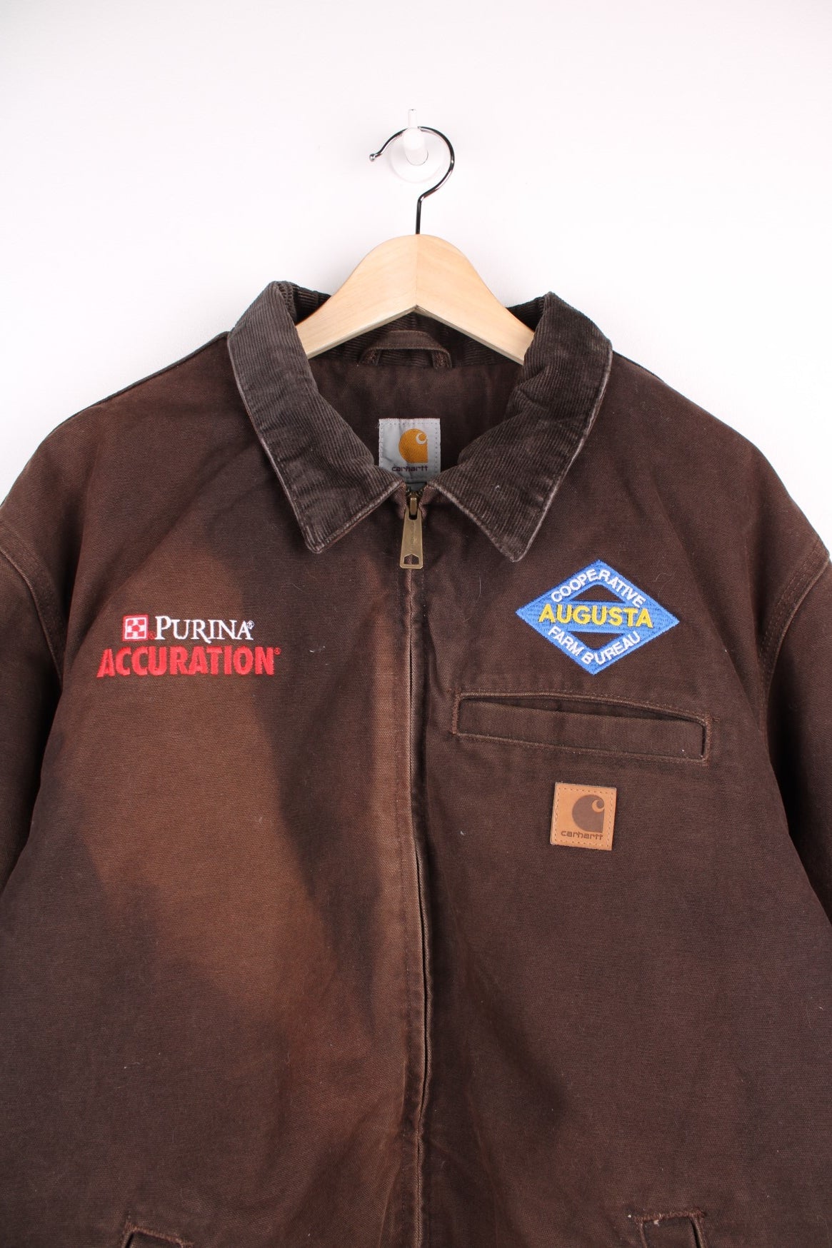 Carhartt Detroit Jacket in a sun burnt brown colourway with a corduroy collar, zips up and has multiple pockets, and company spell out logos embroidered on the front along the Carhartt logo.