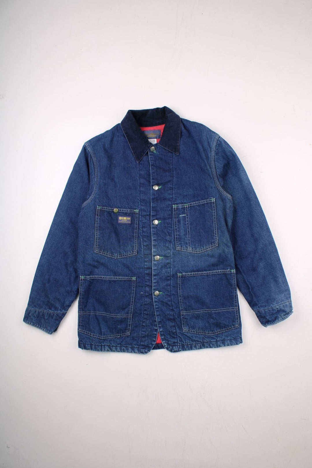 Vintage OshKosh B'Gosh sanforized denim chore jacket in blue with a red quilted lining, four patch pockets, button closure, a corduroy collar, and a small 'OshKosh B'Gosh' logo patch on the front.