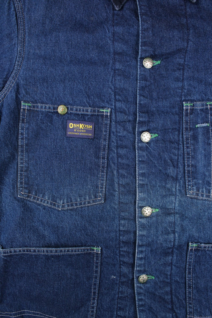 Vintage OshKosh B'Gosh sanforized denim chore jacket in blue with a red quilted lining, four patch pockets, button closure, a corduroy collar, and a small 'OshKosh B'Gosh' logo patch on the front.