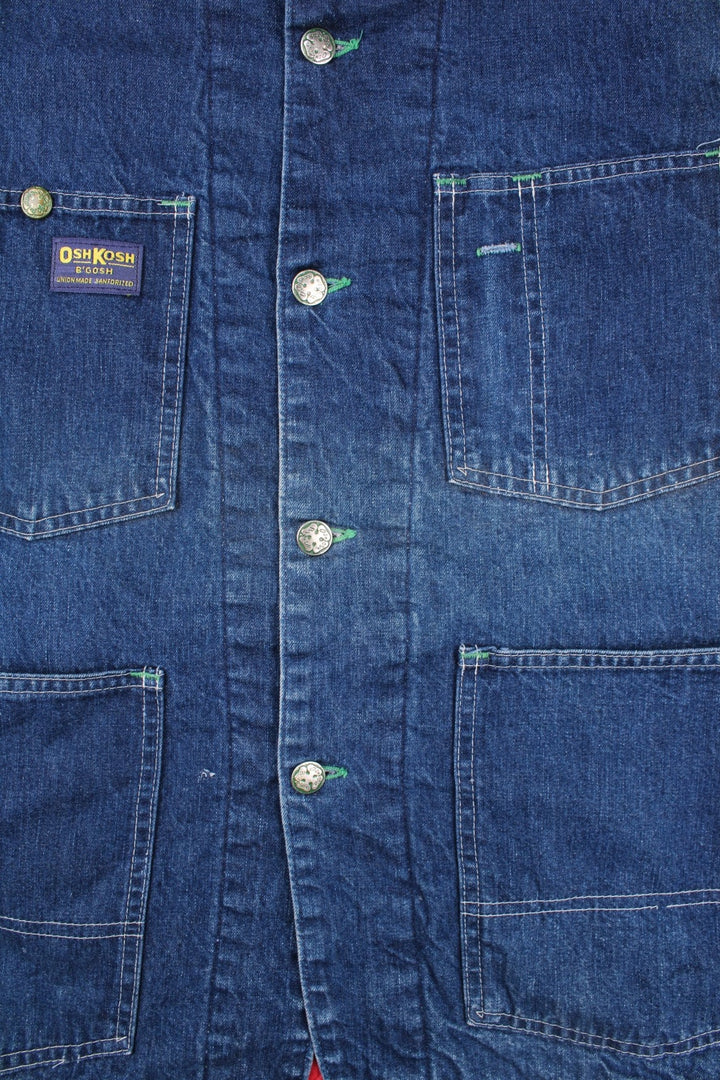 Vintage OshKosh B'Gosh sanforized denim chore jacket in blue with a red quilted lining, four patch pockets, button closure, a corduroy collar, and a small 'OshKosh B'Gosh' logo patch on the front.