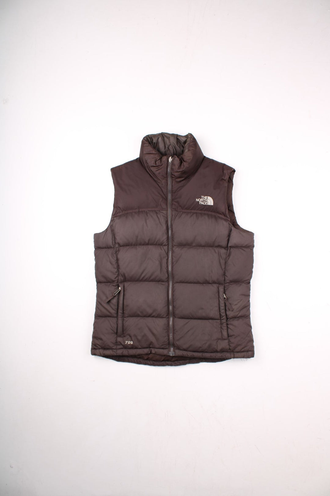 The North Face puffer gilet in brown with zip closure, two zipped pockets, and an embroidered logo in white on the front and back.