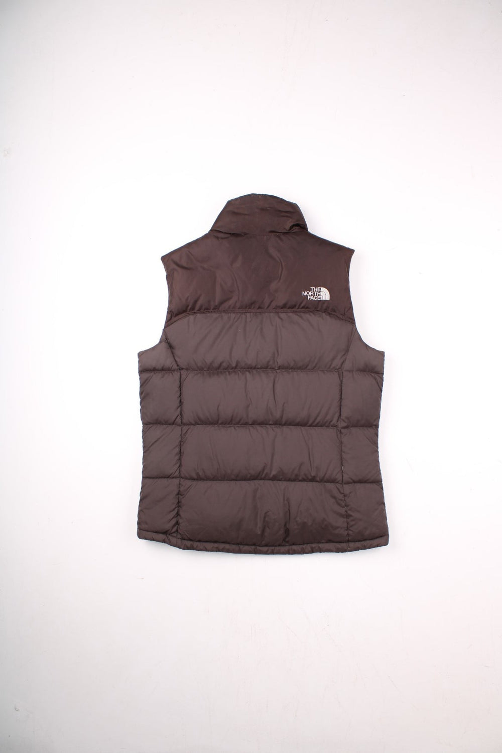 The North Face puffer gilet in brown with zip closure, two zipped pockets, and an embroidered logo in white on the front and back.