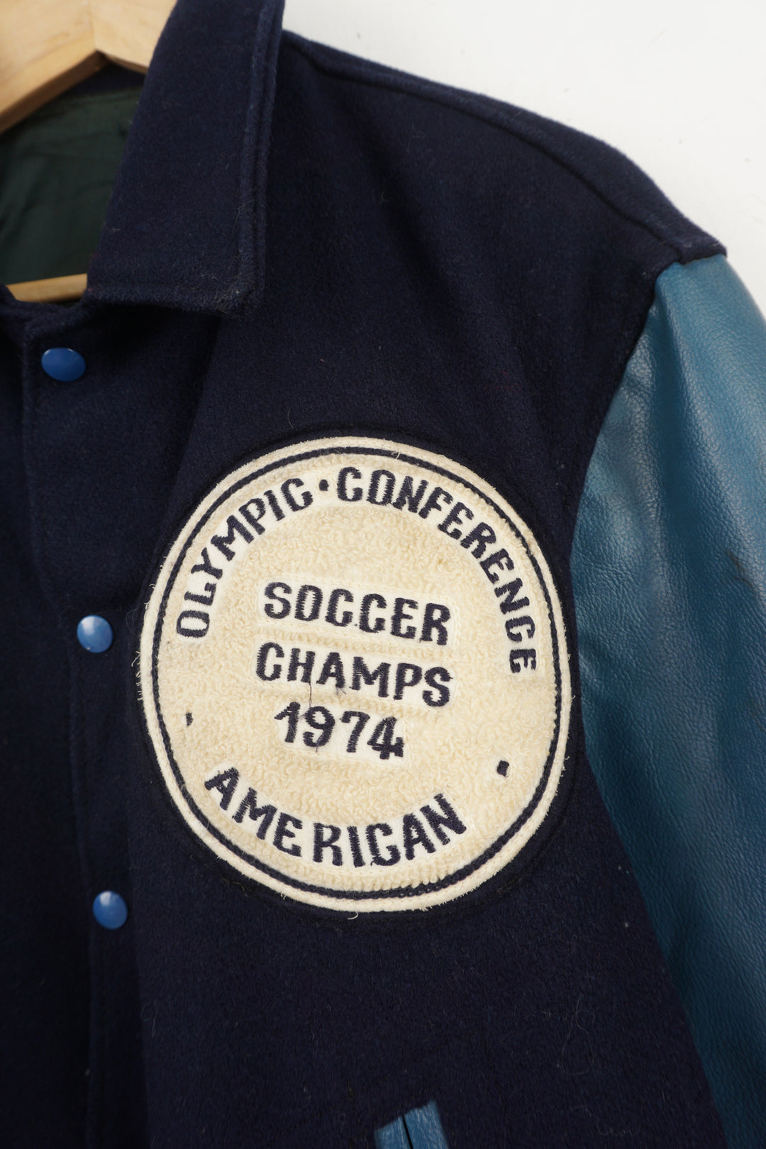 Vintage 1970's Olympic Conference Soccer Champs 1974 blue wool varsity jacket. Features embroidered patch on the front and embroidered spell-out on the back. 