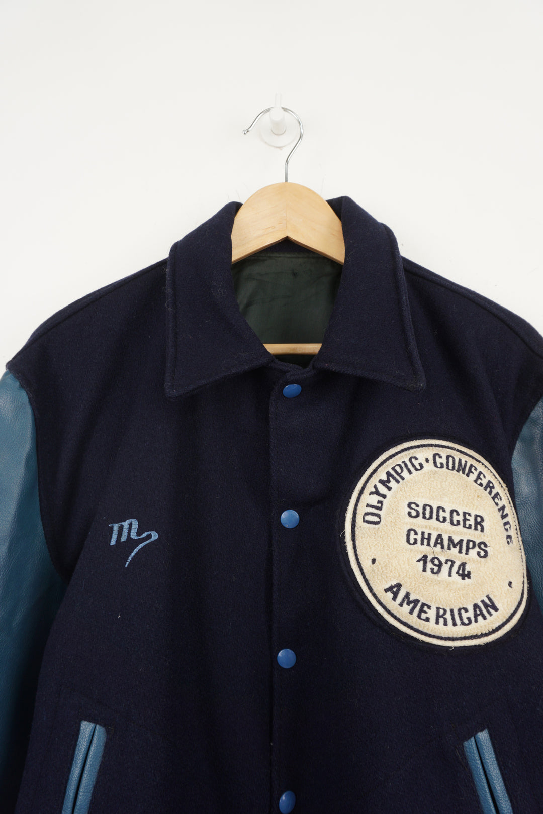 Vintage 1970's Olympic Conference Soccer Champs 1974 blue wool varsity jacket. Features embroidered patch on the front and embroidered spell-out on the back. 