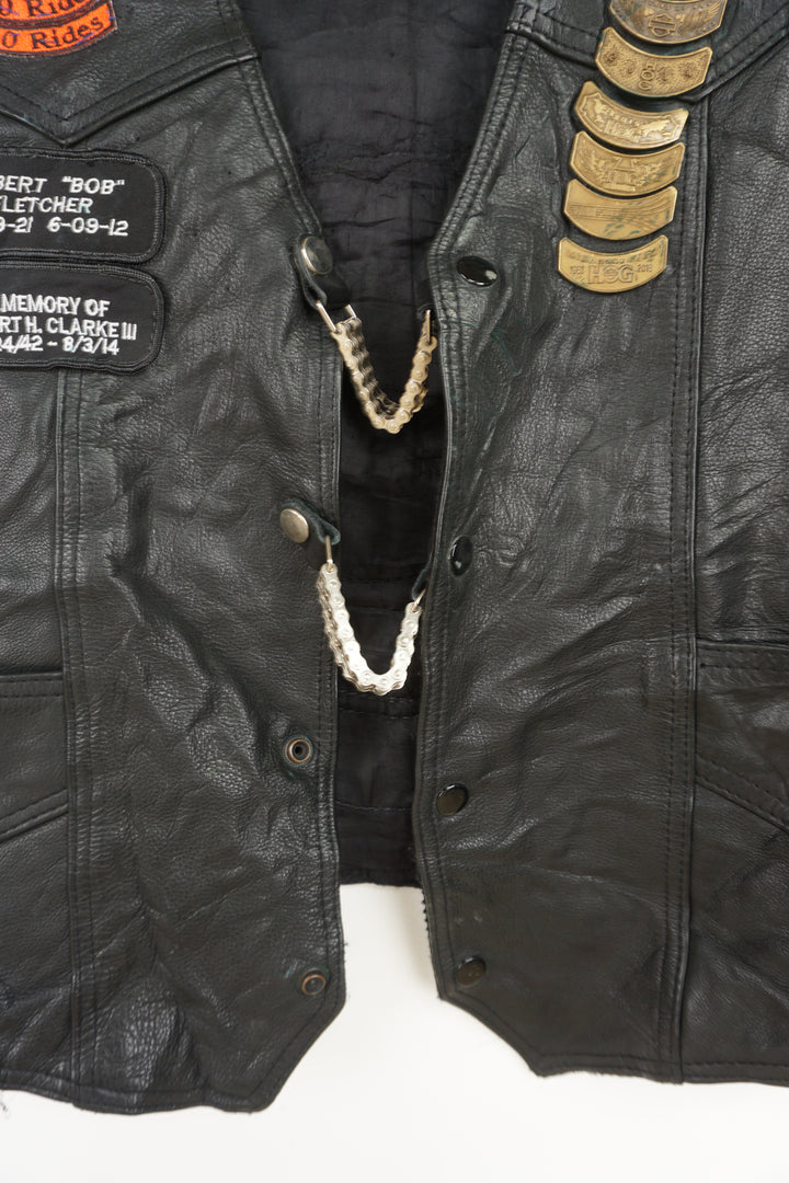 Men's vintage Harley Davidson Owners Group black leather vest with lots of commemorative patches, pins and bike chain details