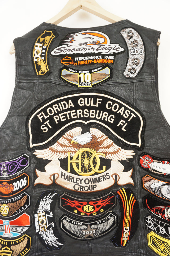 Men's vintage Harley Davidson Owners Group black leather vest with lots of commemorative patches, pins and bike chain details