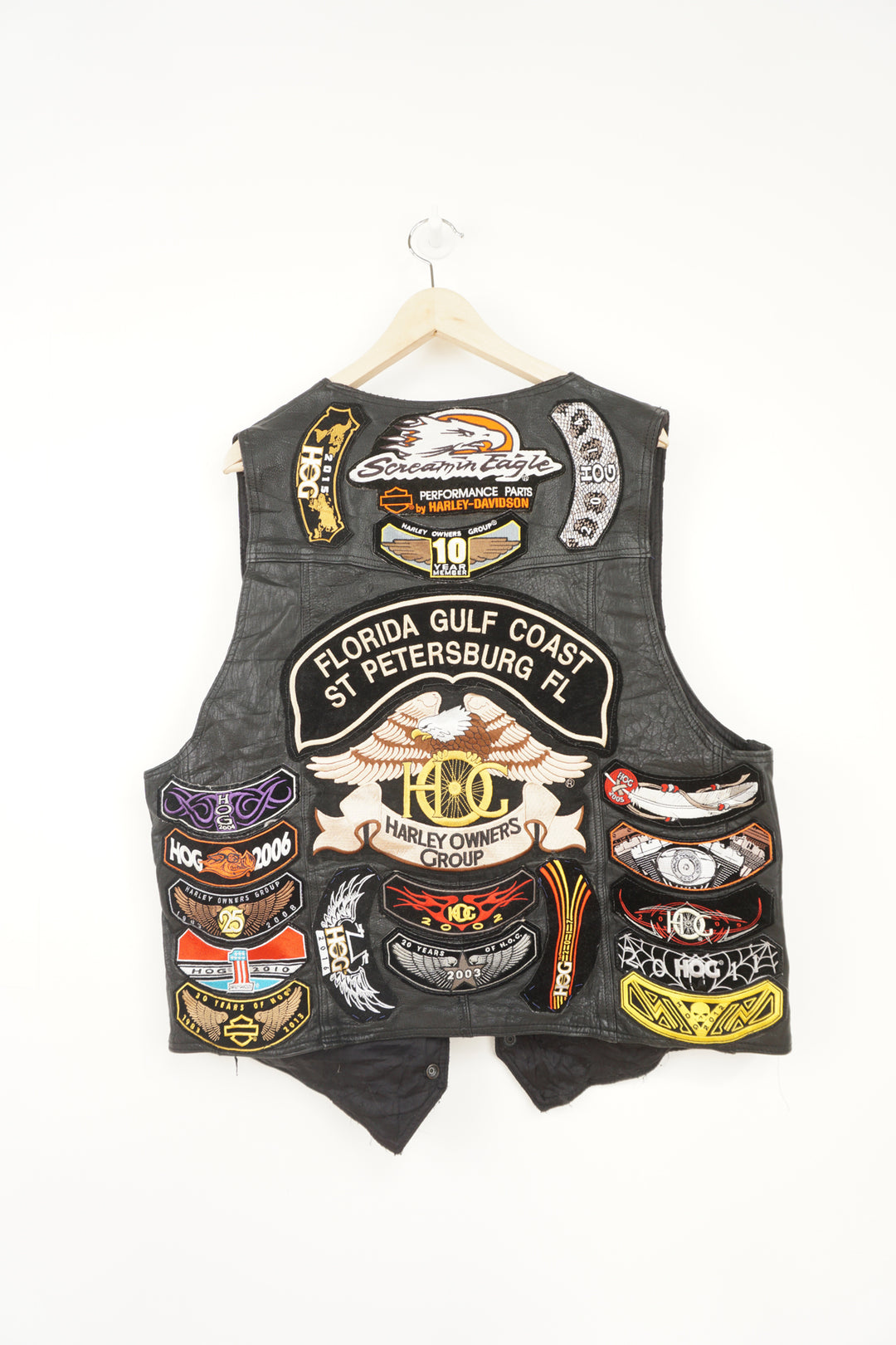 Men's vintage Harley Davidson Owners Group black leather vest with lots of commemorative patches, pins and bike chain details