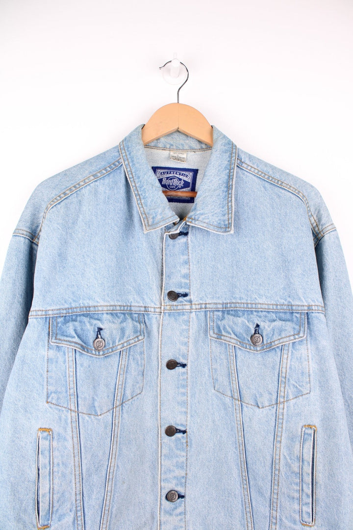 Hard Rock Cafe Denim Jacket in a light blue colourway, button up with multiple pockets, and has the logo embroidered on the back. 