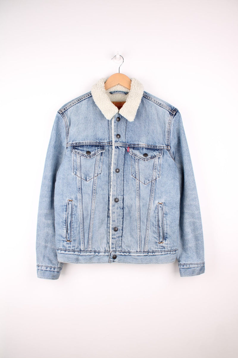 Levi's Sherpa Trucker Jacket in a light blue colourway with a white sherpa lining, button up with multiple pockets, and has the logo embroidered on the front. 