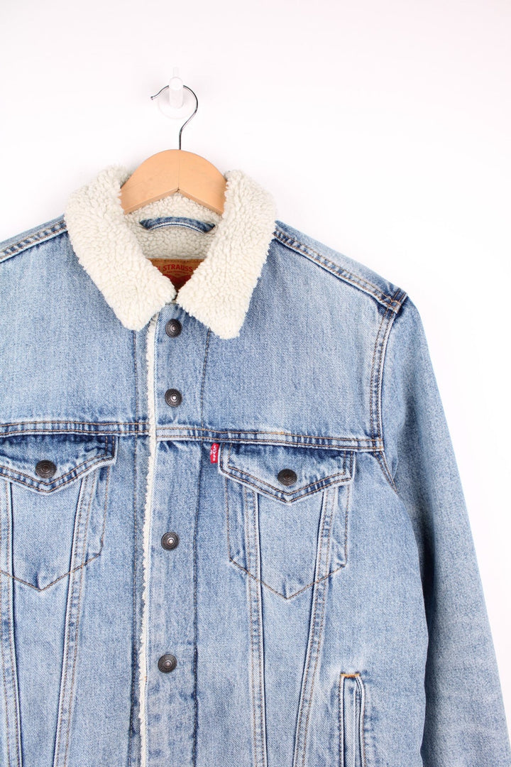 Levi's Sherpa Trucker Jacket in a light blue colourway with a white sherpa lining, button up with multiple pockets, and has the logo embroidered on the front. 