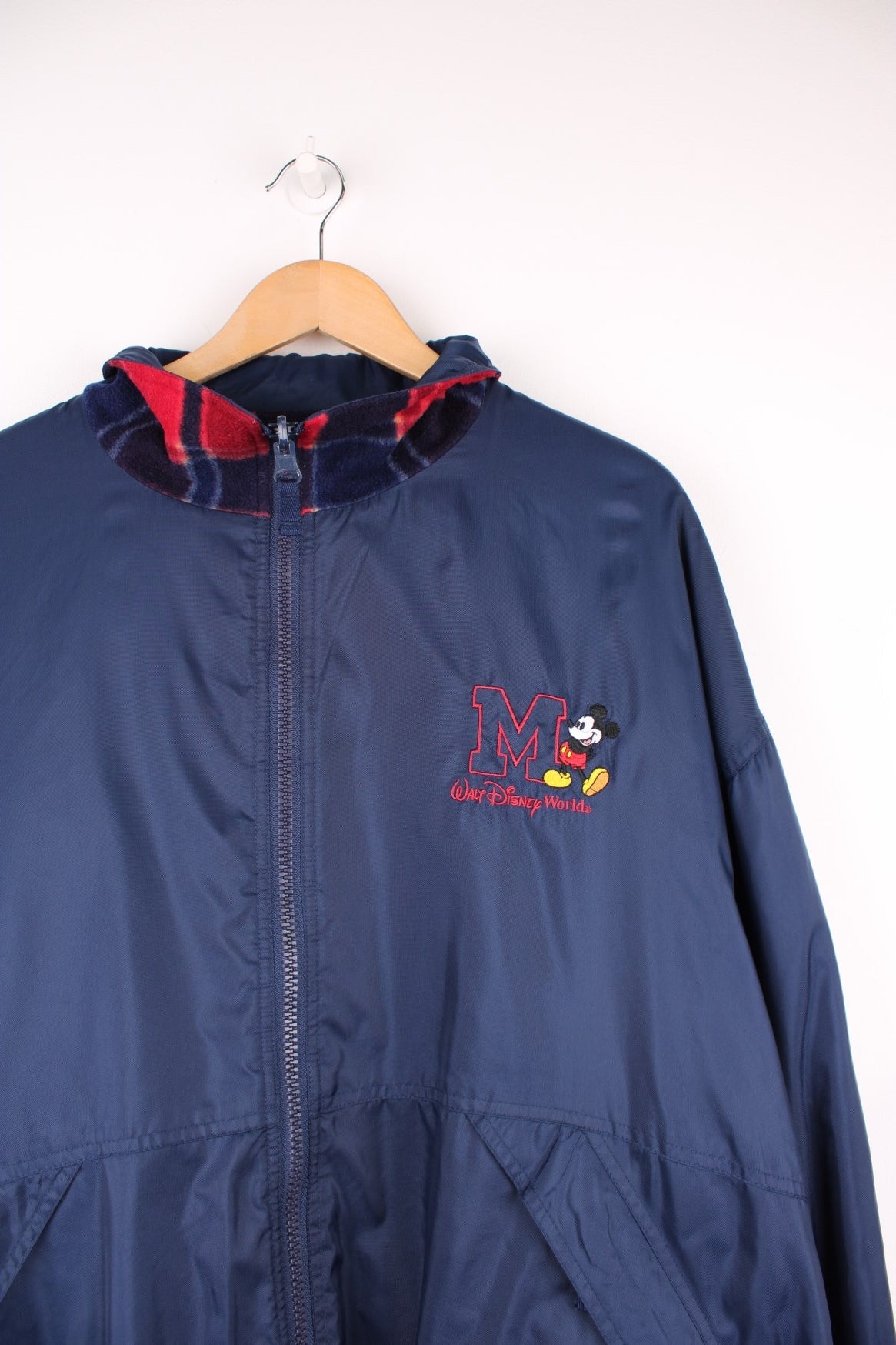 Disney World Reversible Jacket in either a navy blue waterpoof or a tartan fleece colourway, zip up with side pockets, and on the waterproof side has the logo embroidered on the chest. 