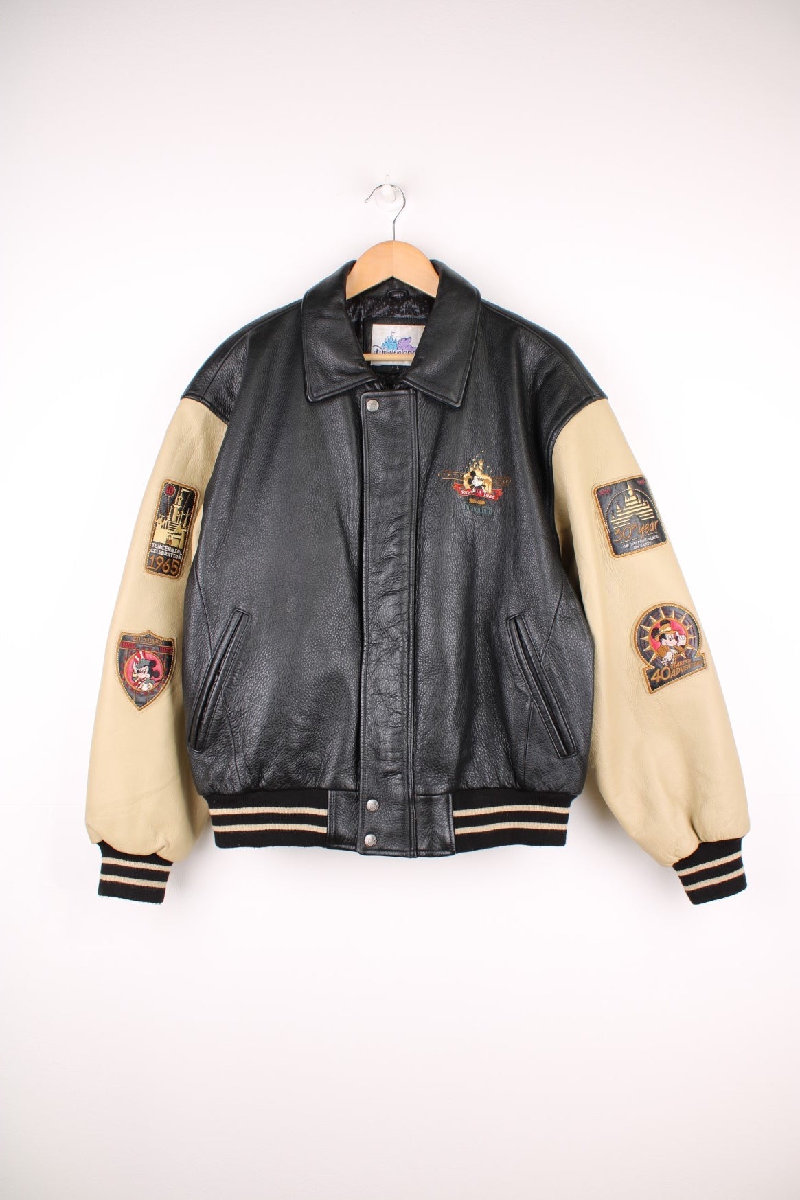 Disneyland Resort 50th Year Anniversary Leather Varsity Jacket in a black and cream colourway, zip up with side pockets, badges going down the sleeves, and has the spell out and Mickey Mouse embroidered on the front and back. 