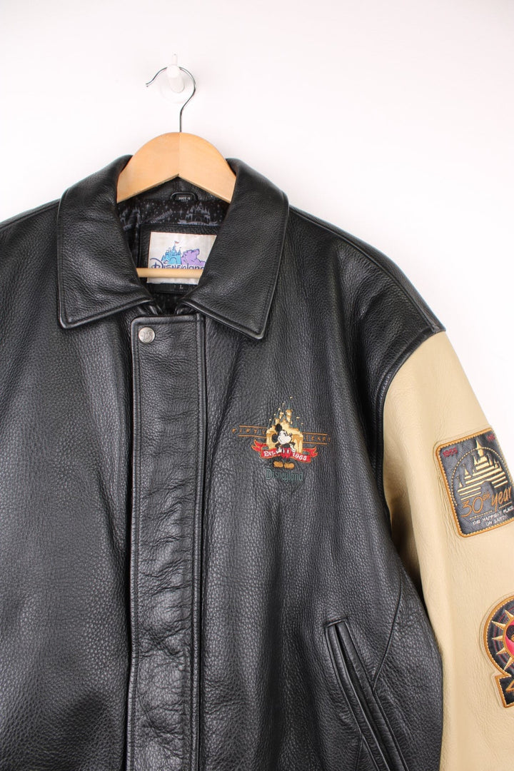 Disneyland Resort 50th Year Anniversary Leather Varsity Jacket in a black and cream colourway, zip up with side pockets, badges going down the sleeves, and has the spell out and Mickey Mouse embroidered on the front and back. 