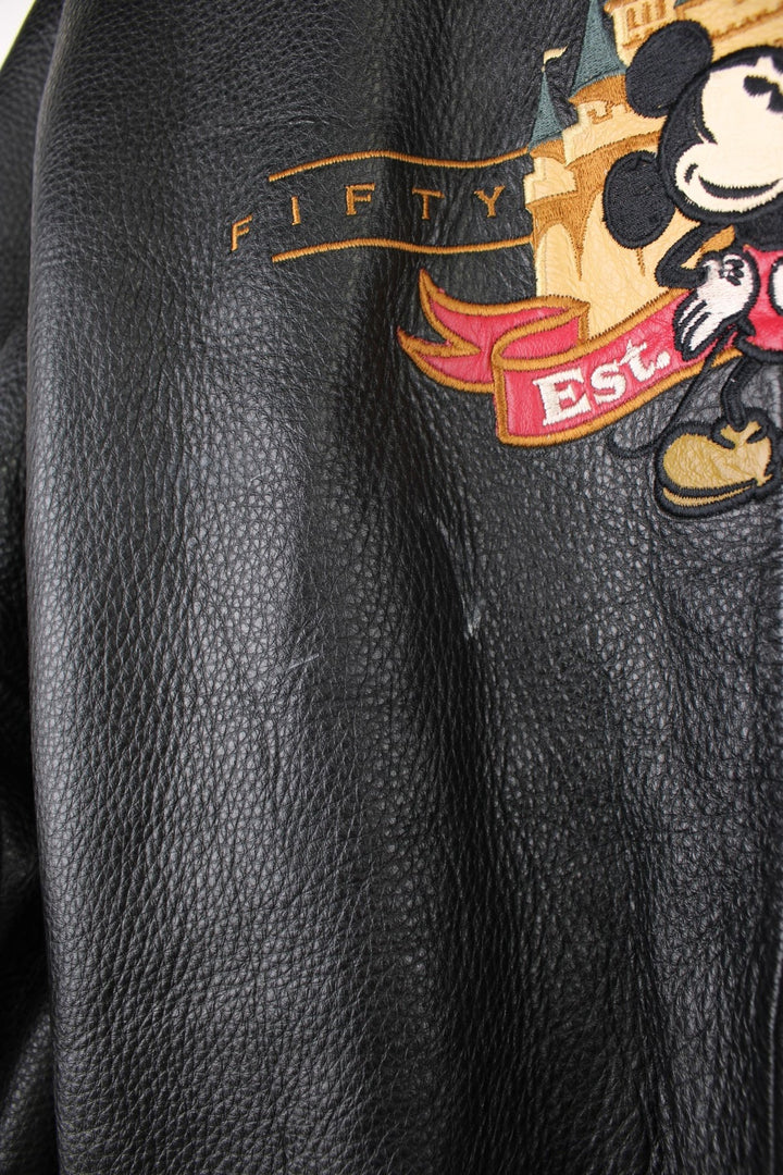 Disneyland Resort 50th Year Anniversary Leather Varsity Jacket in a black and cream colourway, zip up with side pockets, badges going down the sleeves, and has the spell out and Mickey Mouse embroidered on the front and back. 