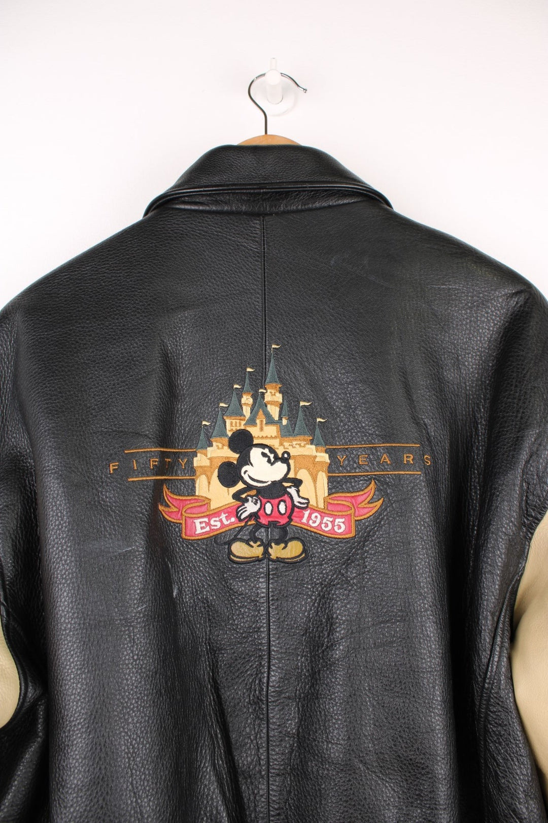 Disneyland Resort 50th Year Anniversary Leather Varsity Jacket in a black and cream colourway, zip up with side pockets, badges going down the sleeves, and has the spell out and Mickey Mouse embroidered on the front and back. 