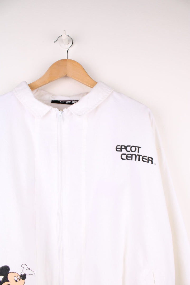 Disney Epcot Center Coach Jacket in a white and black colourway, zip up with side pockets, has a nylon lining, Mickey Mouse and the 'Epcot Centre' spell out printed on the front, and on the back has a variety of countries flag's