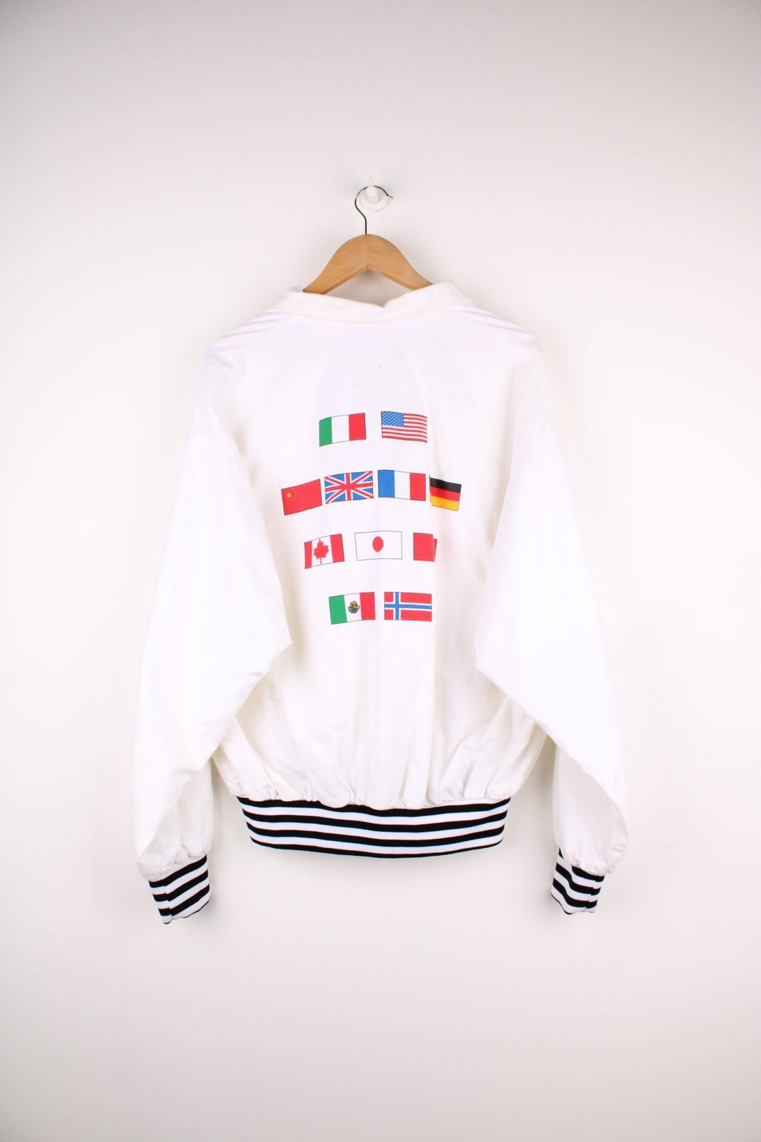 Disney Epcot Center Coach Jacket in a white and black colourway, zip up with side pockets, has a nylon lining, Mickey Mouse and the 'Epcot Centre' spell out printed on the front, and on the back has a variety of countries flag's