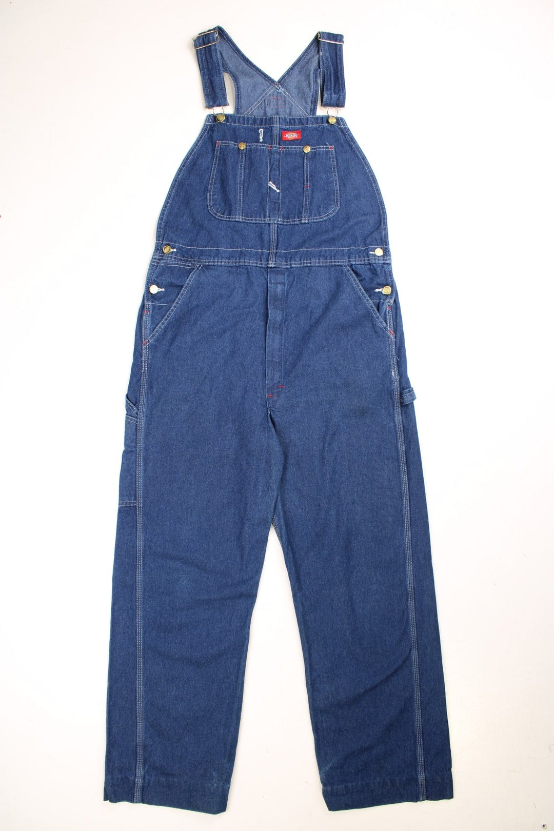 Dickies carpenter-style dungarees in blue denim with multiple pockets, white stitching, and a red logo patch. 