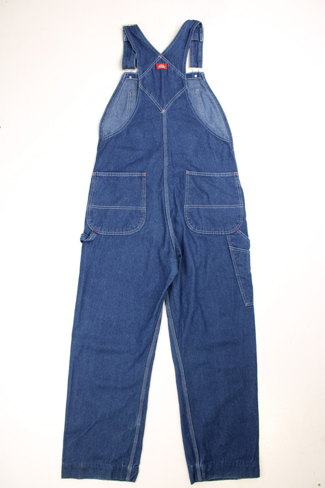 Dickies carpenter-style dungarees in blue denim with multiple pockets, white stitching, and a red logo patch. 