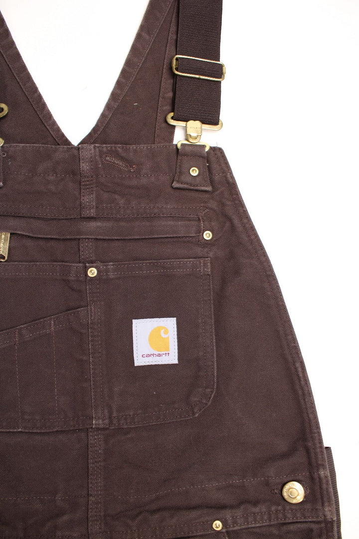 Carhartt carpenter-style dungarees in brown with black straps, multiple pockets, and a logo patch.