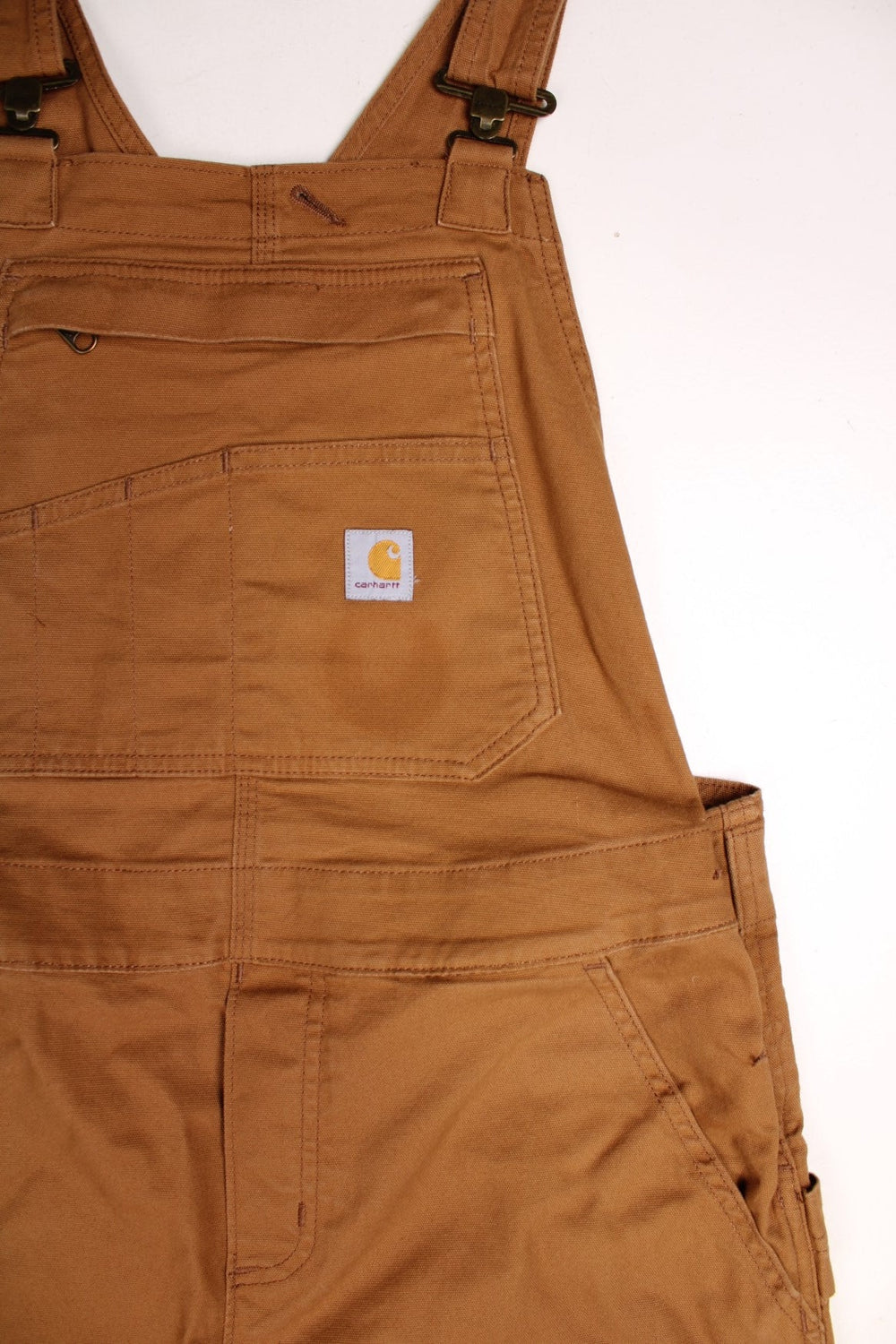 Ochre brown Carhartt carpenter-style dungarees with multiple pockets and sewn-in elastic to expand the waist size. 