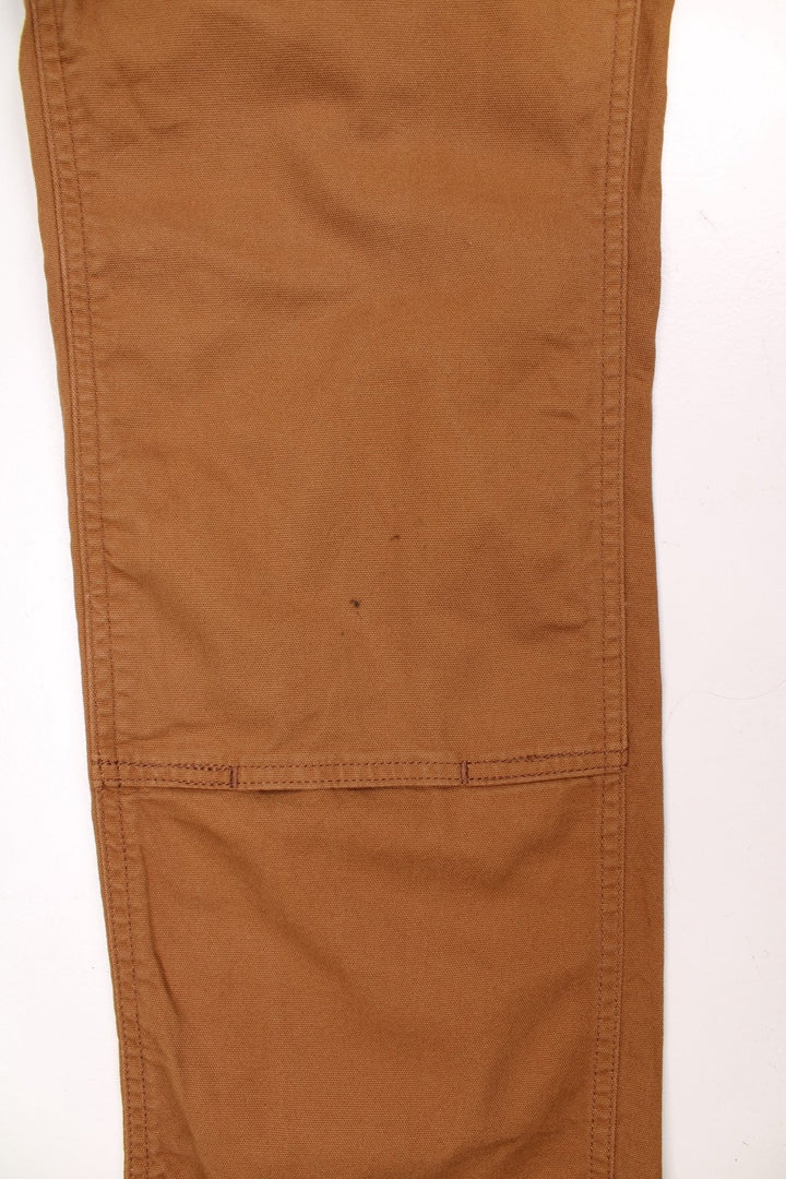 Ochre brown Carhartt carpenter-style dungarees with multiple pockets and sewn-in elastic to expand the waist size. 