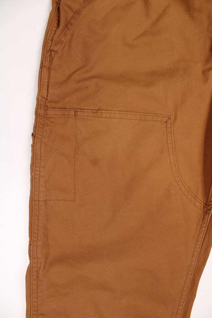 Ochre brown Carhartt carpenter-style dungarees with multiple pockets and sewn-in elastic to expand the waist size. 