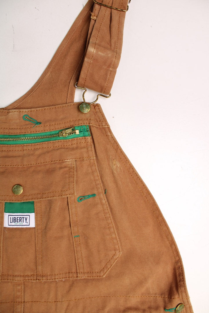 Tan Liberty dungarees with green accents, multiple pockets, logos front and back. 