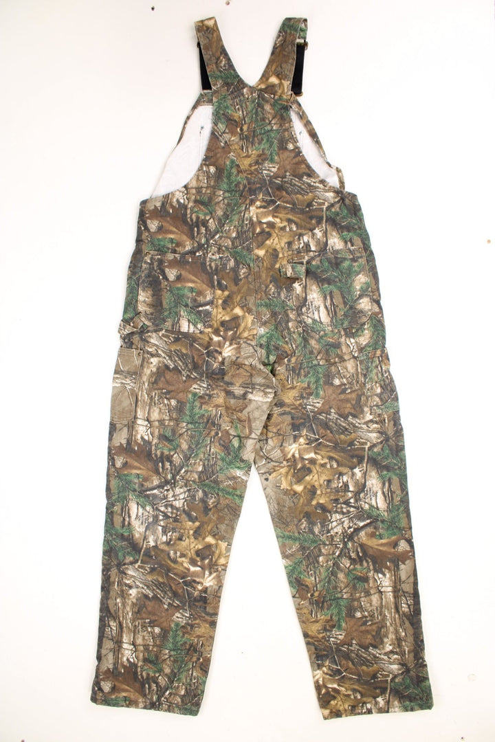 Carhartt double knee duck bib Realtree overalls with quilt lining. Features embroidered leather logo, zip half way up both legs and multiple pockets.