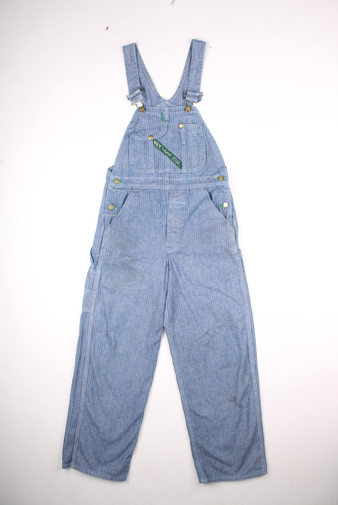 Vintage Key dungarees in blue herringbone denim with multiple pockets, branded hardware, and an embroidered logo patch on the front in green.