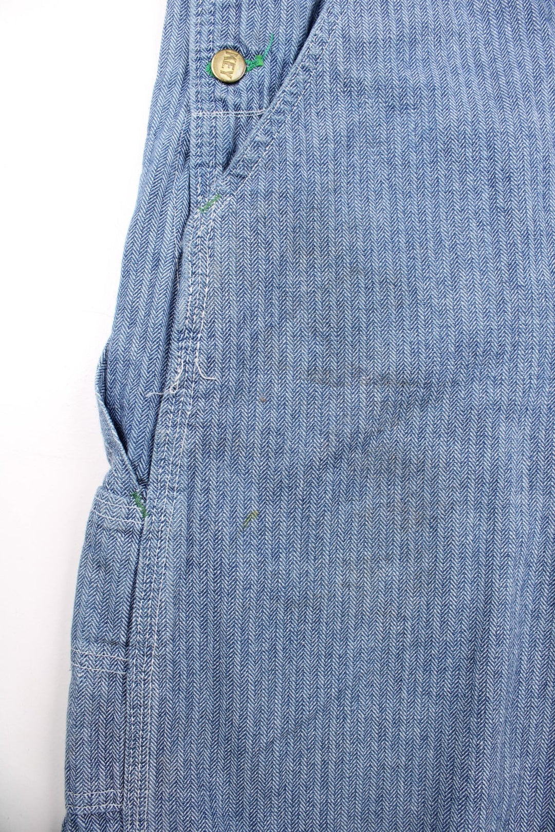 Vintage Key dungarees in blue herringbone denim with multiple pockets, branded hardware, and an embroidered logo patch on the front in green.