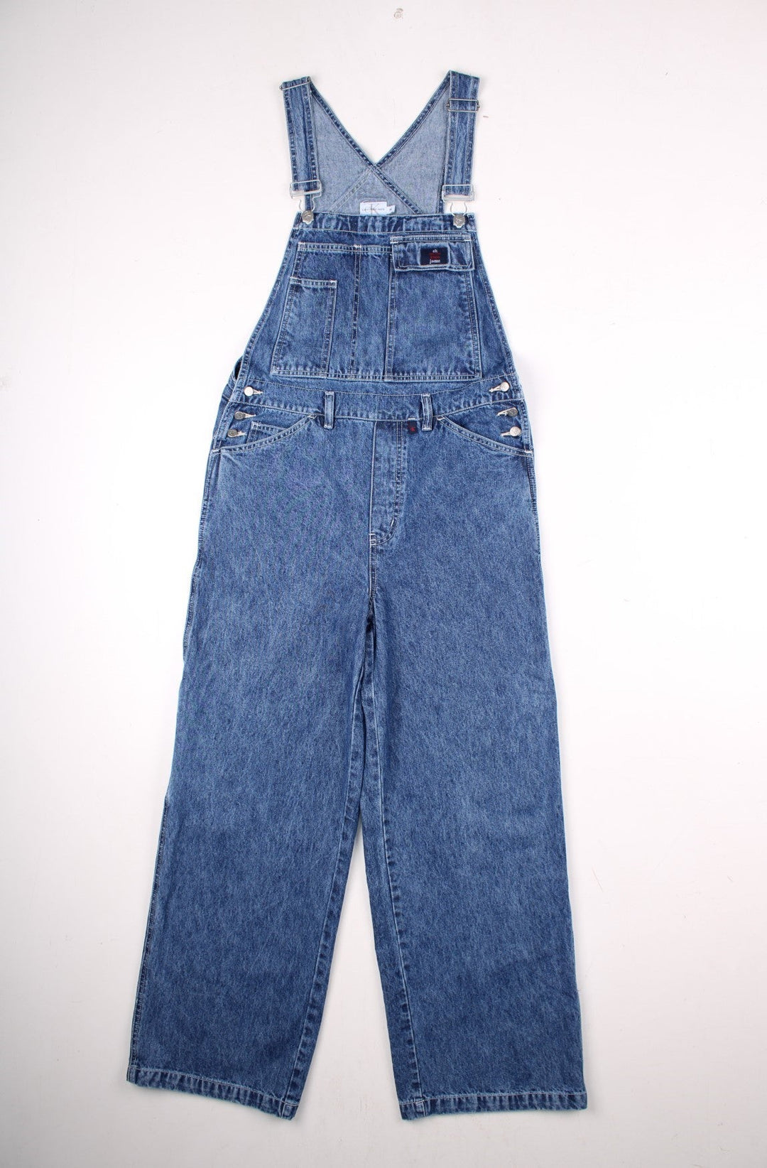 Calvin Klein Jeans denim dungarees in blue with multiple pockets, belt loops, and small logo patches on the front and back.