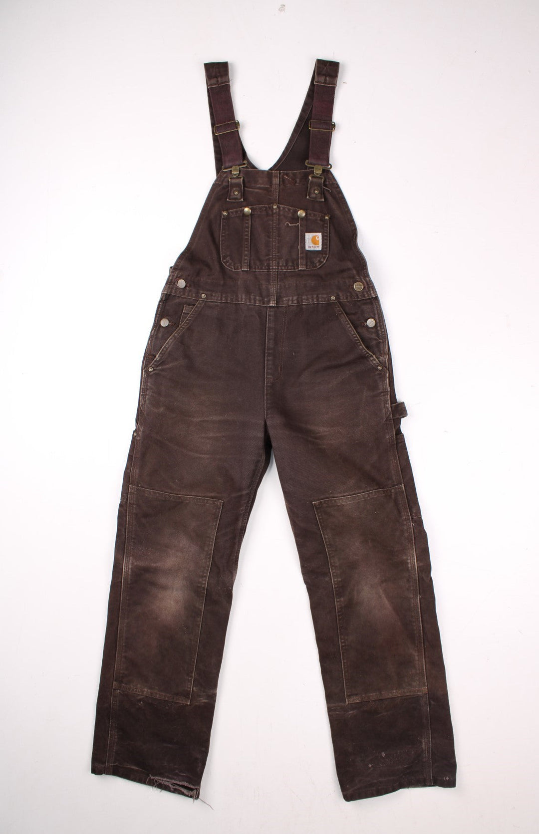 Carhartt carpenter-style dungarees in brown with multiple pockets, red-brown elasticated straps, and a white logo patch on the front.