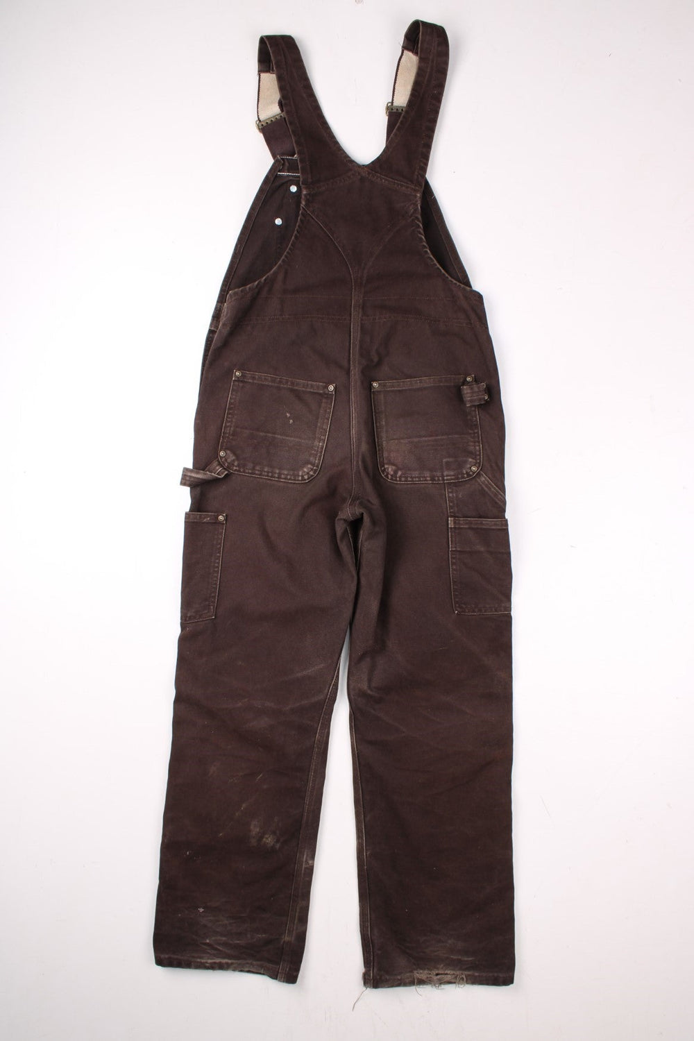 Carhartt carpenter-style dungarees in brown with multiple pockets, red-brown elasticated straps, and a white logo patch on the front.