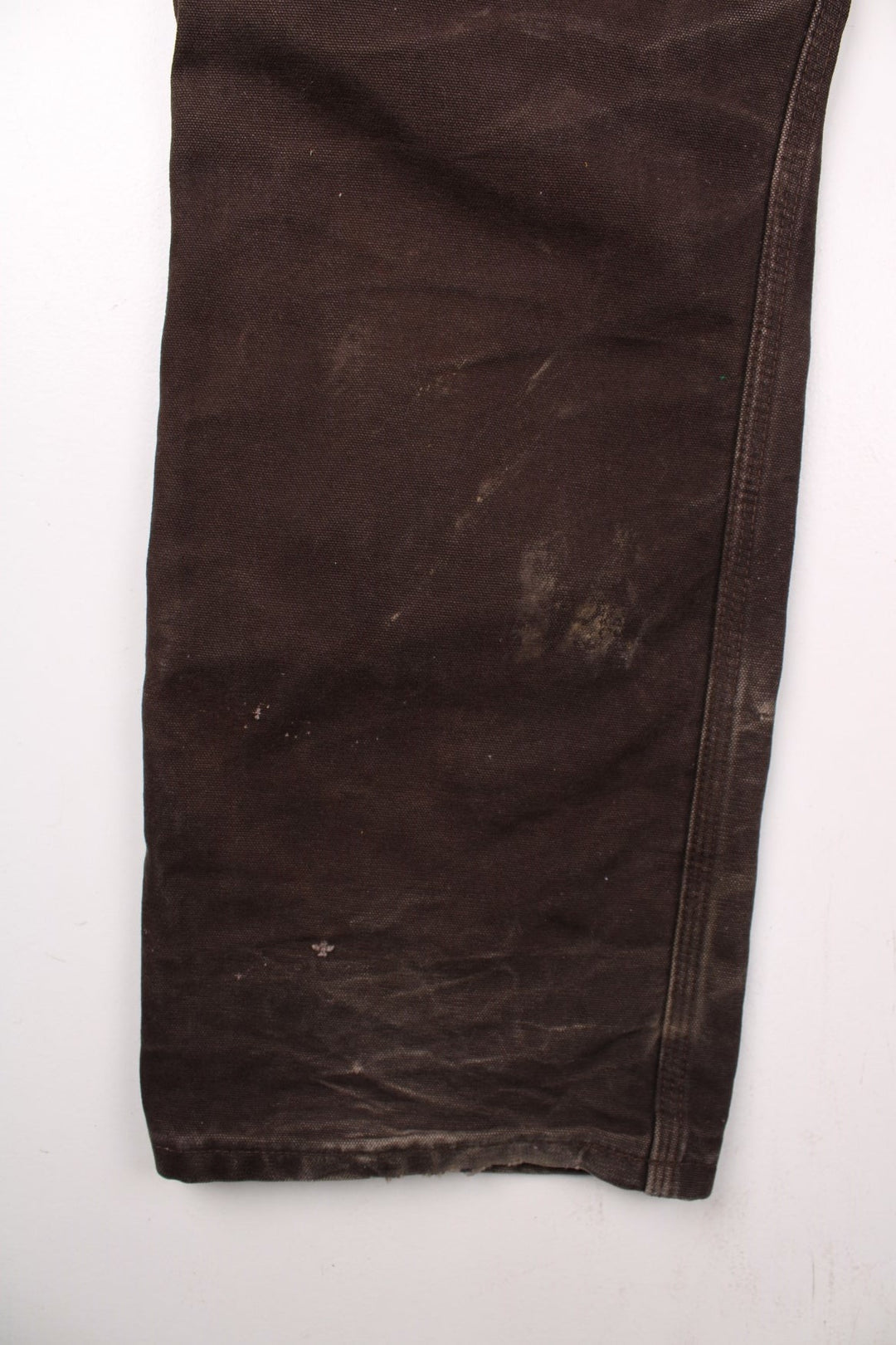 Carhartt carpenter-style dungarees in brown with multiple pockets, red-brown elasticated straps, and a white logo patch on the front.