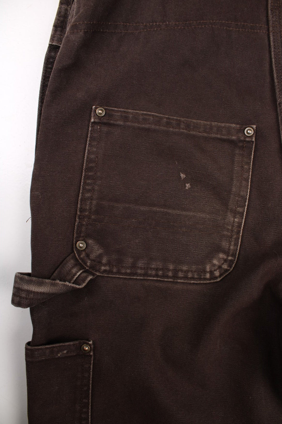 Carhartt carpenter-style dungarees in brown with multiple pockets, red-brown elasticated straps, and a white logo patch on the front.