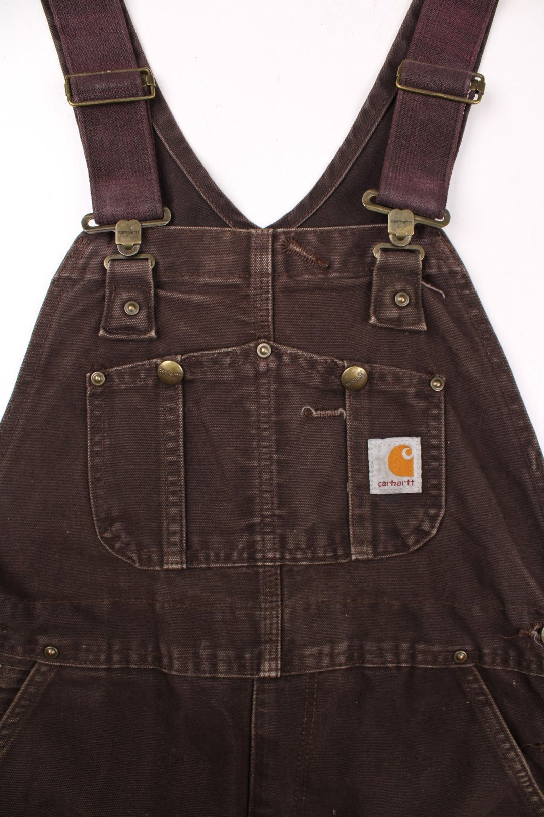 Carhartt carpenter-style dungarees in brown with multiple pockets, red-brown elasticated straps, and a white logo patch on the front.