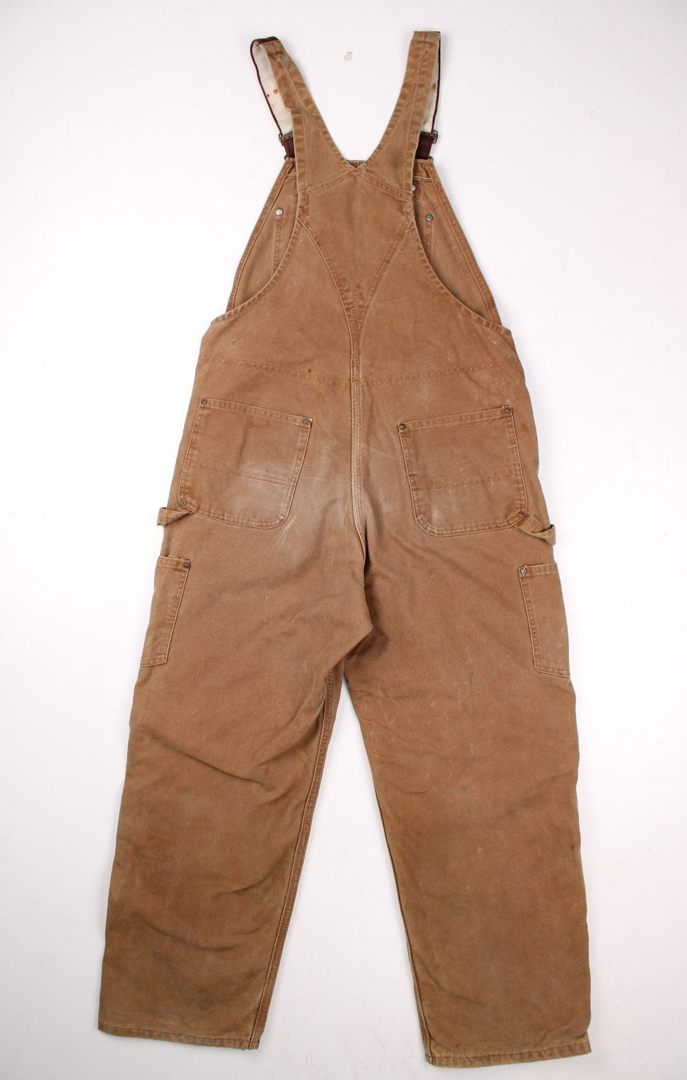 Carhartt carpenter-style dungarees in tan with multiple pockets  red-brown elasticated straps, and a leather logo patch on the front.