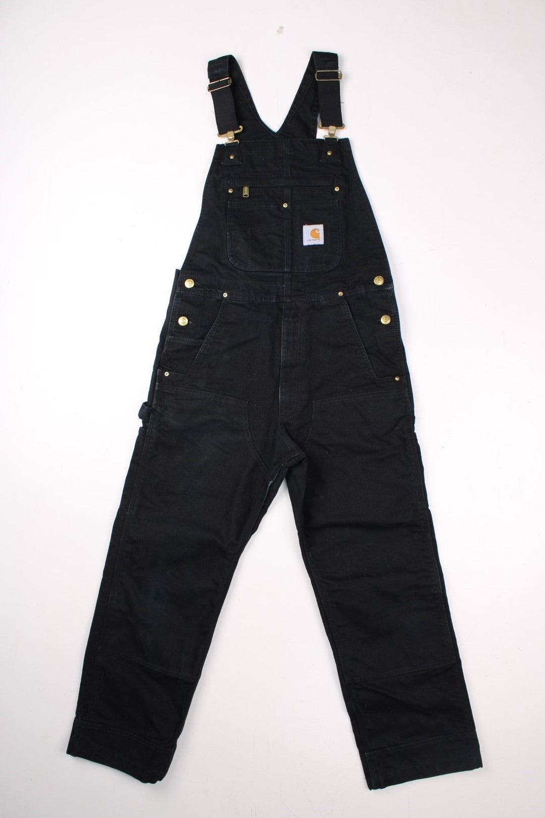 Carhartt dungarees in black with multiple pockets, elasticated straps, elastic panels at the waist, and a white logo patch on the front. .